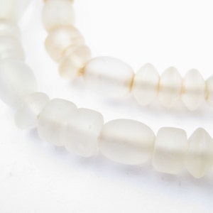 May include: A strand of white glass beads, some round and some with a more irregular shape. The beads are strung on a clear thread.