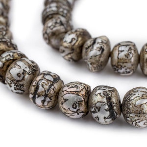 May include: Close-up of a strand of silver-toned beads with a mottled, patterned design. The beads are oval-shaped and strung together, creating a curved line against a white background. The beads have a vintage or antique appearance.
