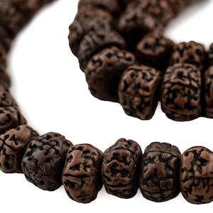 Puede incluir: Un collar de cuentas de mala de madera marrón con intrincados tallados en cada cuenta. Las cuentas están enhebradas con un cordón marrón.