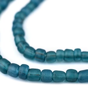 May include: Close-up of a strand of teal-colored, barrel-shaped beads. The beads have a slightly irregular shape and a matte finish. The beads are strung together, creating a necklace or bracelet.