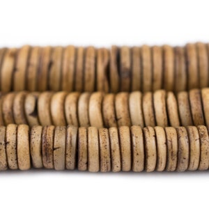 May include: Close-up of a strand of natural wood beads. The beads are light brown with a slightly darker brown color in the center. The beads are arranged in a staggered pattern.