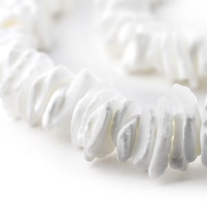 May include: A close-up of a white shell necklace. The necklace is made of small, irregular shaped shells that are strung together on a white cord.