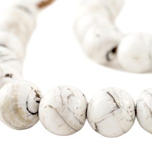 May include: Close-up of a white beaded bracelet with a marbled pattern. The beads are round and have gray and brown veining. The bracelet is on a white background.