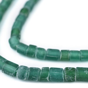 以下が含まれることがあります： 緑色のガラスビーズのストランドのクローズアップ。ビーズは丸みを帯びたエッジを持つ円筒形で、わずかに半透明の外観をしています。ビーズは一緒にひもでつながれており、ネックレスまたはブレスレットを作成しています。