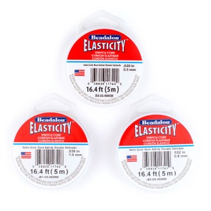 Puede incluir: Tres carretes de cord&oacute;n el&aacute;stico Beadalon Elasticity de color blanco, con etiquetas rojas. Las etiquetas muestran el logotipo de Beadalon y el texto "Elasticity Stretch Cord Cordon Elastique Cordon Elastico". Las etiquetas tambi&eacute;n indican el grosor del cord&oacute;n en pulgadas y mil&iacute;metros, as&iacute; como la longitud del cord&oacute;n en pies y metros. Las etiquetas est&aacute;n impresas con un c&oacute;digo de barras y el texto "Solo para uso de adultos."