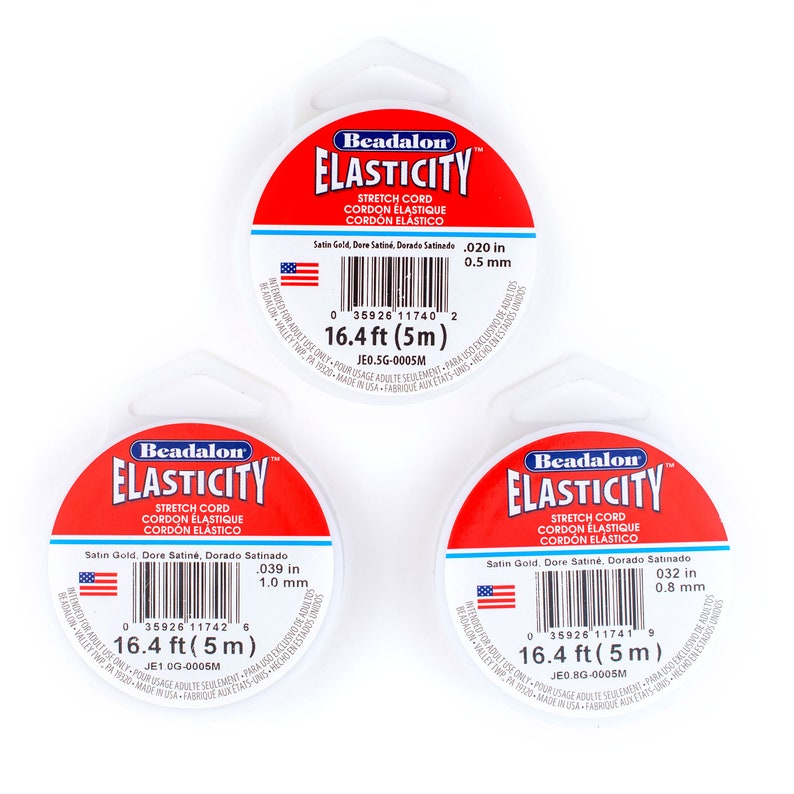 Puede incluir: Tres carretes de cord&oacute;n el&aacute;stico Beadalon Elasticity de color blanco, con etiquetas rojas. Las etiquetas muestran el logotipo de Beadalon y el texto "Elasticity Stretch Cord Cordon Elastique Cordon Elastico". Las etiquetas tambi&eacute;n indican el grosor del cord&oacute;n en pulgadas y mil&iacute;metros, as&iacute; como la longitud del cord&oacute;n en pies y metros. Las etiquetas est&aacute;n impresas con un c&oacute;digo de barras y el texto "Solo para uso de adultos."