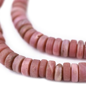 Op de afbeelding: Een streng van cirkelvormige, schijfvormige kralen in verschillende tinten oudroze en gedempt roze. Elke kraal heeft een gladde, matte textuur met subtiele natuurlijke variaties in kleur en oppervlaktekenmerken, gerangschikt in een lijn.
