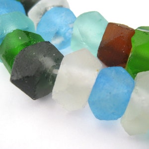 Puede incluir: Una hebra de cuentas de vidrio de colores, con tonos de azul, verde, marrón y blanco. Las cuentas tienen una forma irregular y una apariencia ligeramente mate.