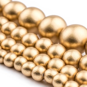 K&ouml;nnte beinhalten: Nahaufnahme einer goldfarbenen Perlenkette. Die Perlen sind rund und glatt und in einem versetzten Muster angeordnet. Die Perlen sind aus Holz und haben eine matte Oberfl&auml;che.