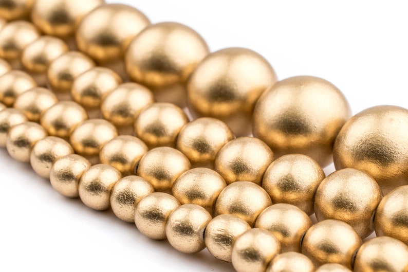 K&ouml;nnte beinhalten: Nahaufnahme einer goldfarbenen Perlenkette. Die Perlen sind rund und glatt und in einem versetzten Muster angeordnet. Die Perlen sind aus Holz und haben eine matte Oberfl&auml;che.