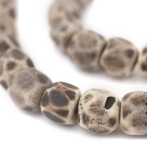 May include: A close-up of a necklace made of brown and white speckled beads. The beads are round and have a rough texture.