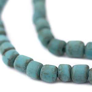 May include: Close-up of a strand of turquoise-colored, square-shaped beads. The beads have a slightly weathered appearance, with variations in color and texture. The beads are strung together, creating a necklace or bracelet.