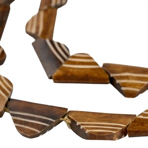May include: A necklace composed of multiple brown wooden beads, each featuring a distinct trapezoidal shape. The beads are decorated with three thin, light-colored horizontal stripes on their surface and are strung together on a thin cord.