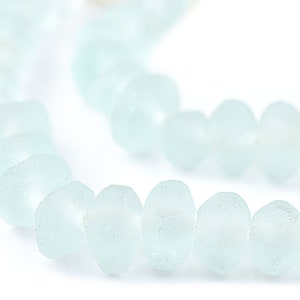 May include: A close-up of a strand of pale blue, frosted glass beads. The beads are oval-shaped and have a slightly irregular surface. The beads are strung together, possibly for a necklace or bracelet. The background is white.