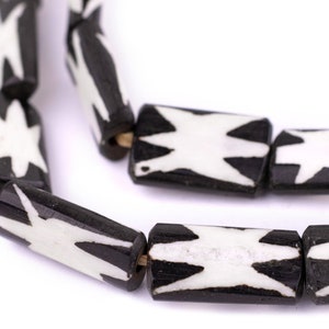 May include: Close-up of a strand of black and white beads. The beads are cylindrical with a starburst design in white against a black background. The beads are strung together with a visible string.
