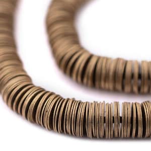 May include: Close-up of a necklace made of numerous small, round, bronze-colored metal discs. The discs are strung together, forming a flexible, circular shape. The necklace is set against a white background, highlighting the metallic sheen and texture of the jewelry.