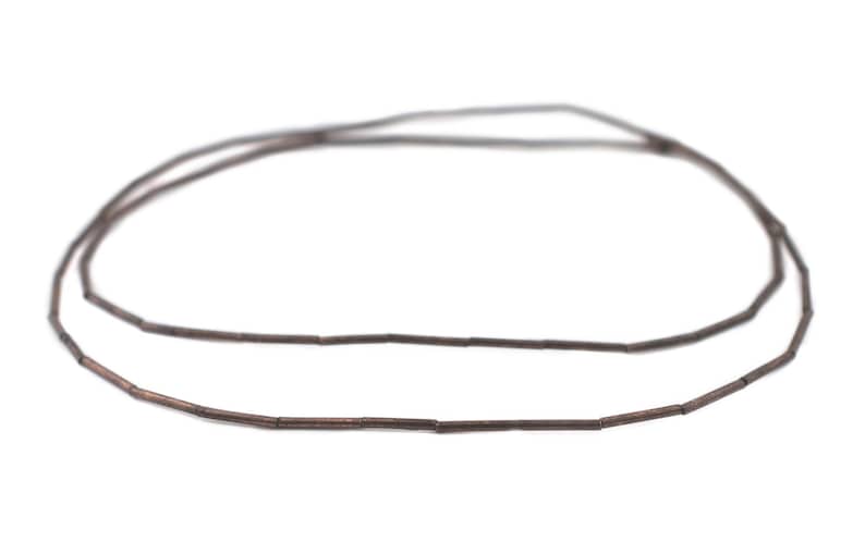Pu&ograve; includere: Una collana di perline di metallo marrone, ogni perlina &egrave; un piccolo cilindro. Le perline sono infilate per formare una collana.