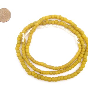 May include: A strand of yellow glass beads, similar in size to a US penny, is coiled on a white surface.