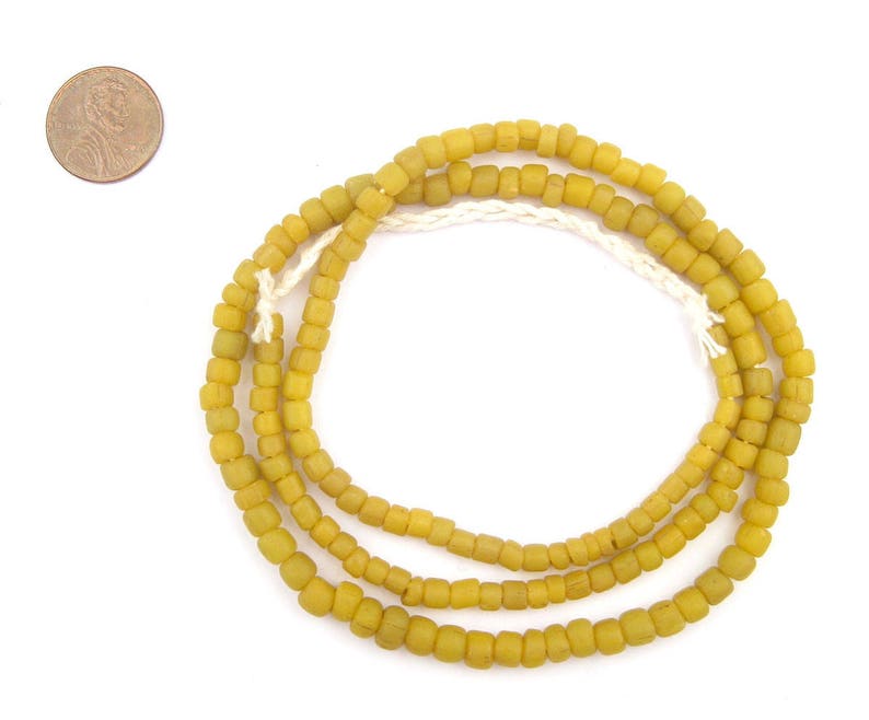 May include: A strand of yellow glass beads, similar in size to a US penny, is coiled on a white surface.