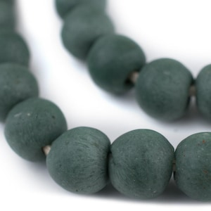 Puede incluir: Una hebra de cuentas de madera verde oscuro, ensartadas con un cordón delgado. Las cuentas son redondas y tienen una superficie ligeramente texturizada.