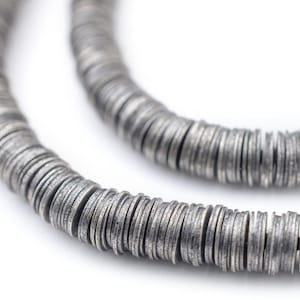 May include: Close-up of a silver-colored necklace made of small, flat, circular beads. The beads are strung together to form a flexible chain. The necklace is set against a white background.
