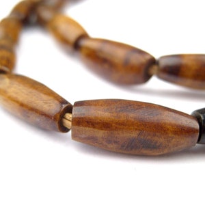 May include: A close-up of a brown wooden bead necklace. The beads are oval-shaped and have a natural wood grain pattern.