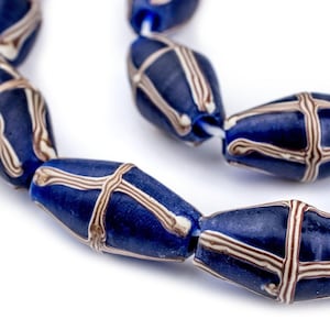 May include: A strand of dark blue glass beads with a cross-like design in white and brown. The beads are oval-shaped and strung together on a white string, perfect for jewelry making.