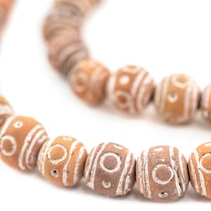 May include: A strand of brown clay beads with white geometric patterns. The beads are strung together on a cord and are arranged in a circular pattern.