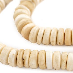 Op de afbeelding: Close-up van een ketting gemaakt van ronde, gebroken witte kralen. De kralen hebben een natuurlijke, organische uitstraling met kleurvariaties, variërend van licht crèmekleurig tot een iets donkerdere bruintint. De ketting wordt getoond tegen een witte achtergrond.