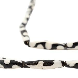 Puede incluir: Un collar de cuentas cilíndricas con un patrón en blanco y negro. Las cuentas están enhebradas para formar una cadena larga y continua.