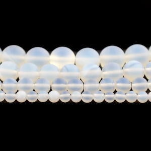 May include: A strand of white moonstone beads, with varying sizes, arranged in a graduated pattern. The beads are smooth and have a subtle shimmer.