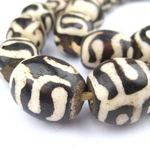 Könnte beinhalten: Eine Kette aus schwarzen und weißen gemusterten Knochenperlen. Die Perlen sind oval geformt und haben eine glatte, polierte Oberfläche.