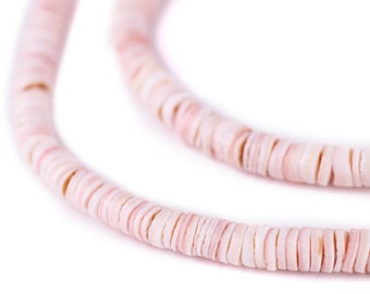 Op de afbeelding: Close-up van een ketting gemaakt van platte, ronde, lichtroze en witte schelpkralen. De kralen zijn aan elkaar geregen, waardoor een gebogen lijn ontstaat tegen een witte achtergrond. De ketting is een natuurlijk, strandachtig accessoire.