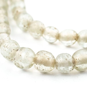 May include: Close-up of a strand of clear, round beads with a slightly irregular shape. The beads have a speckled, textured appearance and are strung together, creating a curved line against a white background. The beads are approximately 0.5 inches in diameter.