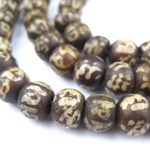 Può includere: Una collana di mala di legno marrone con lettere bianche su ogni perla. Le perle sono rotonde e hanno una finitura liscia e lucida.
