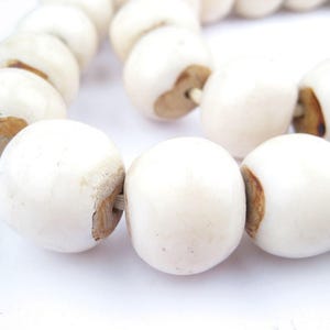 May include: A strand of white ceramic beads with brown accents. The beads are round and smooth, and they are strung together on a white cord.