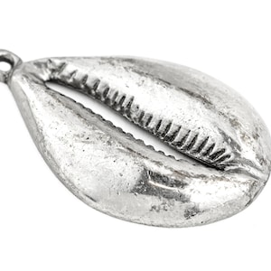 May include: A silver-colored cowrie shell pendant with a textured surface and a loop for hanging. The shell has a detailed, ridged opening and a slightly weathered appearance, suggesting an antique or vintage style. Ideal for jewelry making.