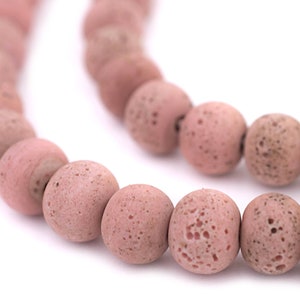 May include: A strand of pink lava rock beads. The beads are round and have a rough, textured surface.