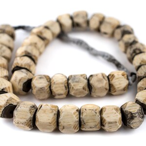 May include: A string of beige bone beads with a dark grey string threaded through them. The beads are faceted and have a worn, rustic look.