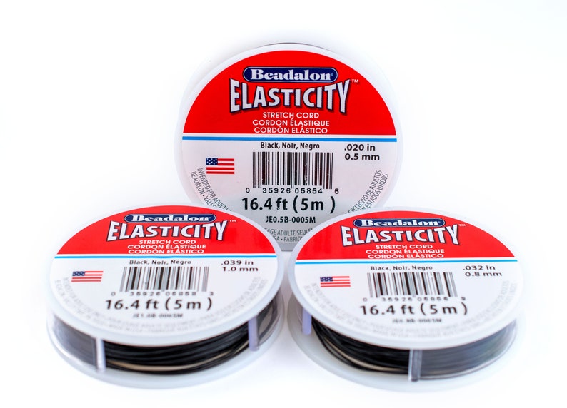 Puede incluir: Tres carretes de cord&oacute;n el&aacute;stico Beadalon Elasticity negro, cada uno con una etiqueta blanca y una pancarta roja que dice "Beadalon Elasticity". Las etiquetas indican el grosor del cord&oacute;n en pulgadas y mil&iacute;metros, y la longitud del cord&oacute;n en pies y metros. Los carretes est&aacute;n sobre una superficie blanca.