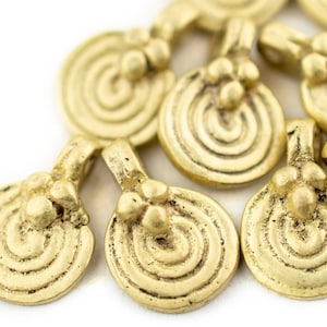 Può includere: Primo piano di diversi ciondoli in metallo color oro. Ogni ciondolo presenta un design a spirale su una base circolare, con un piccolo anello e tre perline decorative nella parte superiore. I ciondoli sono disposti su uno sfondo bianco.