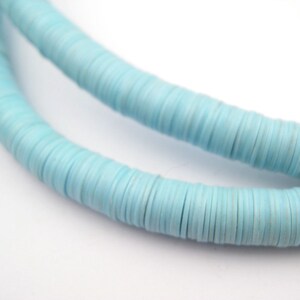 Peut inclure: Un brin de perles rondes en argile polymère bleu clair. Les perles sont plates et empilées les unes sur les autres pour former un long brin.