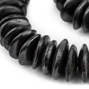 May include: A close-up of a black wooden necklace featuring unique, faceted beads. The beads are smooth and polished, giving a sleek and contemporary look.