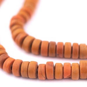 May include: Close-up of a necklace made of small, round, orange beads. The beads have a natural, earthy appearance with variations in color, ranging from light orange to a deeper, reddish-brown. The necklace is displayed against a white background.