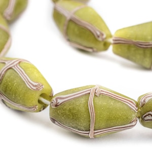 May include: Close-up of a strand of olive-green glass beads. Each bead is an elongated oval shape, wrapped with a crisscross pattern of thin, light brown stripes. The beads are strung together, creating a curved line against a white background.