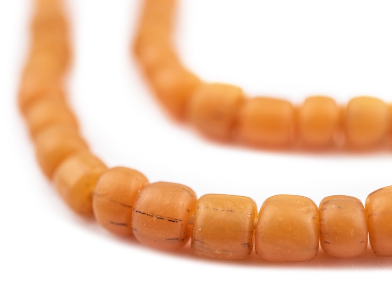 K&ouml;nnte beinhalten: Nahaufnahme einer orangefarbenen Perlenkette. Die Perlen sind rund und haben eine leicht strukturierte Oberfl&auml;che.