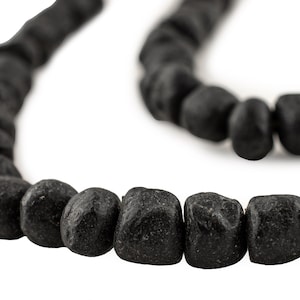 May include: A close-up of a black necklace with irregularly shaped beads. The beads have a rough, textured surface and are strung together to form a necklace. The background is white, highlighting the dark color of the beads.