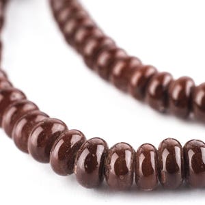 Pode incluir: Um colar de contas marrons com contas redondas e brilhantes. As contas são enfiadas juntas em um laço contínuo.