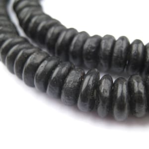 May include: Close-up of a strand of dark grey wooden beads. The beads are cylindrical with a slightly ridged texture, strung together to form a necklace or bracelet. The background is plain white, highlighting the beads.