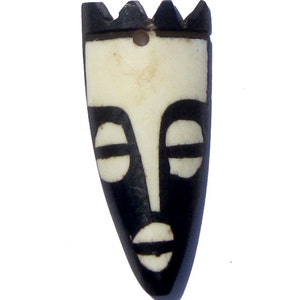 May include: Black and white carved wooden pendant in the shape of a face. The face has a crown on top and simple features.